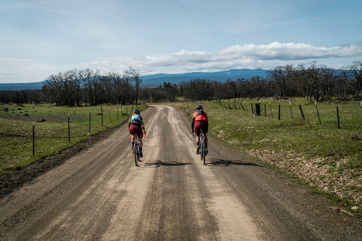 two people riding bikes down a dirt road